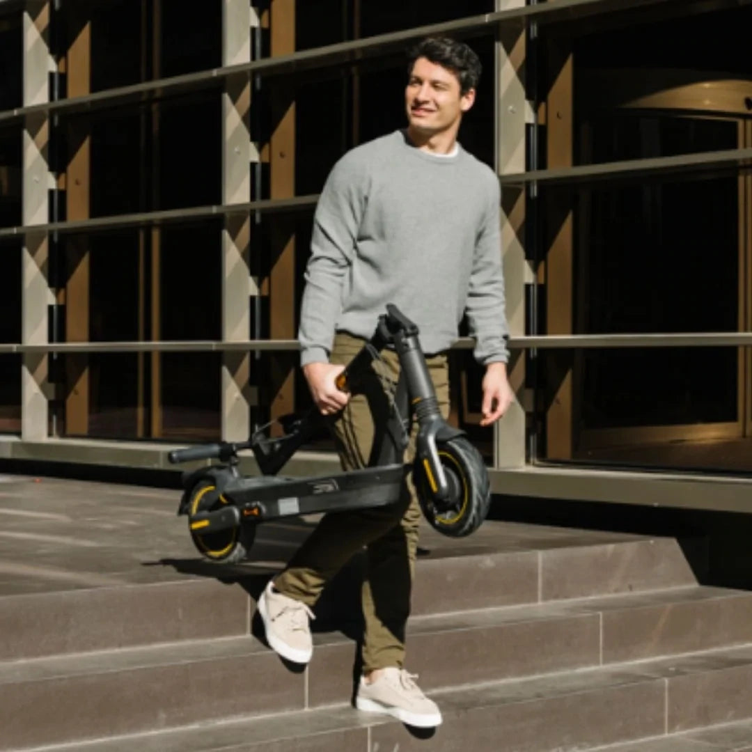 Man carrying folded Segway Ninebot Max G2 scooter down steps in an urban setting