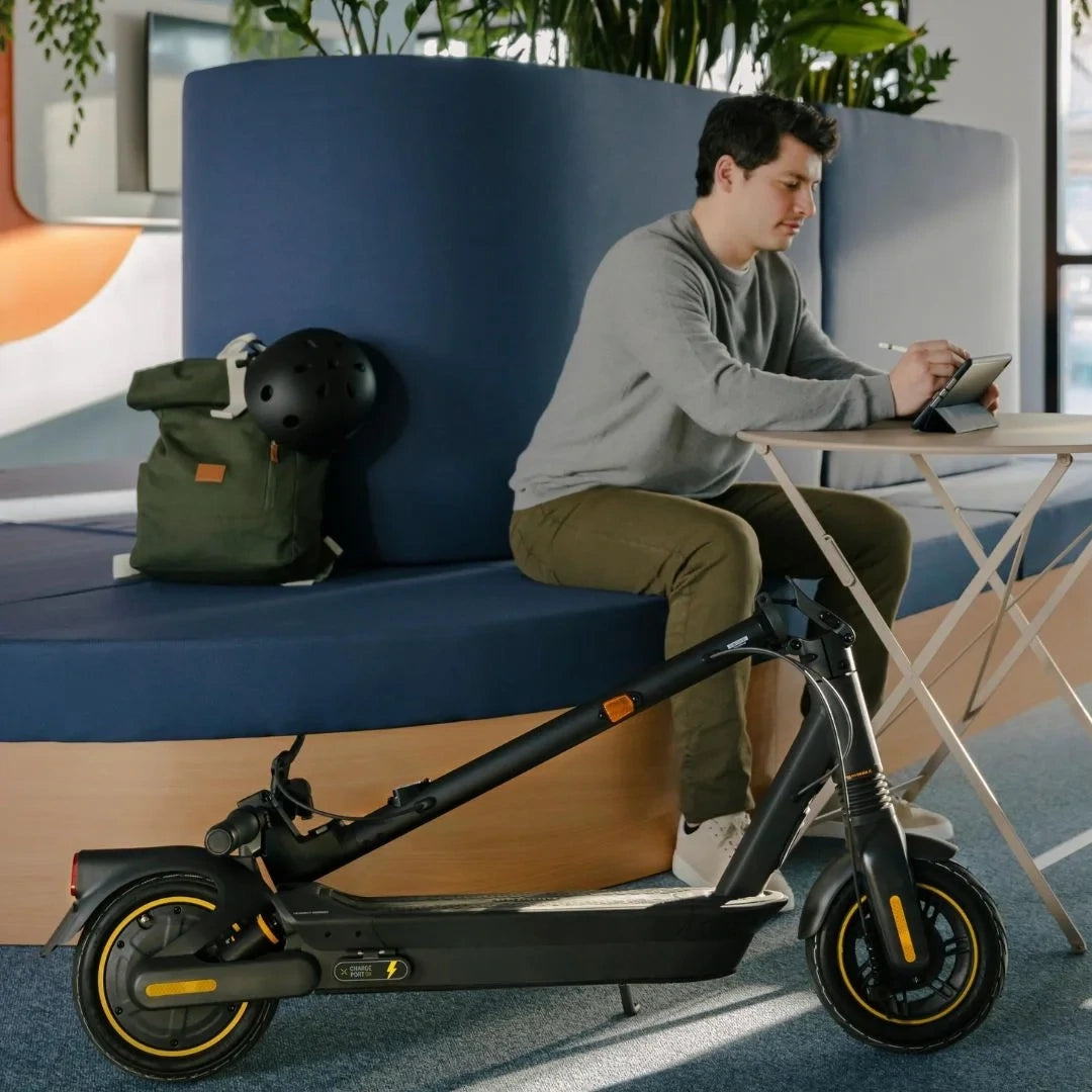Man working at a desk in public space with the Segway Ninebot KickScooter Max G2 parked beside him