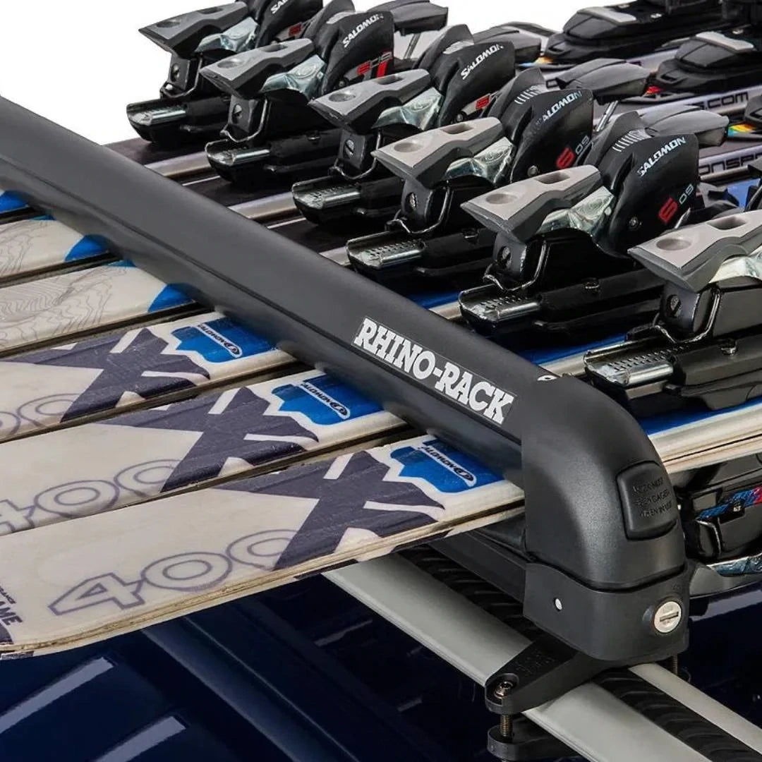 Angled side view of multiple skis held in a Rhino-Rack carrier on top of a roof rack system.