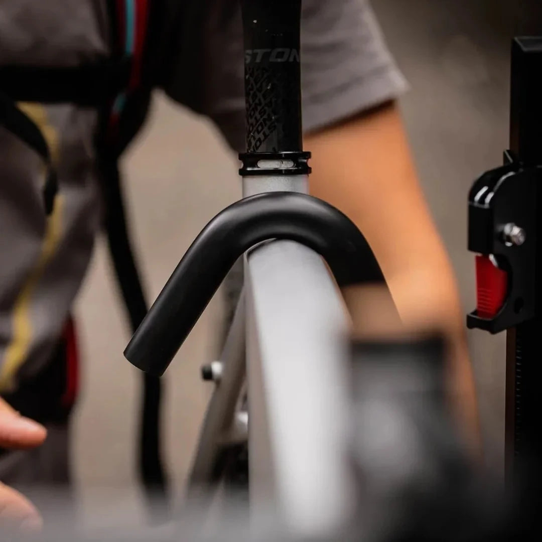 Close-up of a Swagman XTC2 Tilt bike rack securing a bicycle by the front wheel with a padded hook arm and ratcheting mechanism.
