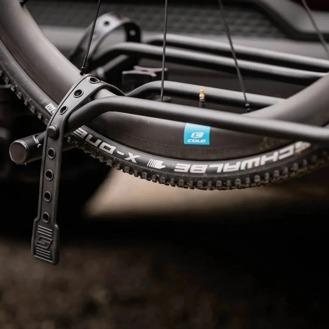 Close-up of a bike tire secured in a Swagman XTC2 Tilt bike rack using a rubberized strap over the wheel on a Schwalbe X-One tire.