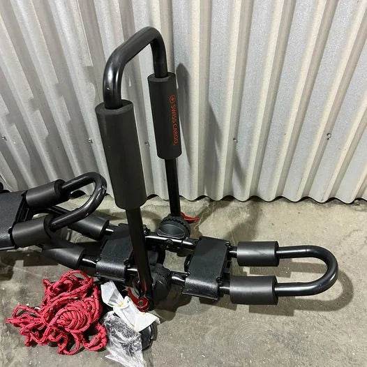 Swiss Cargo 3-in-1 Kayak Carrier laid on ground showing foam pads, mounting hardware, and red straps.