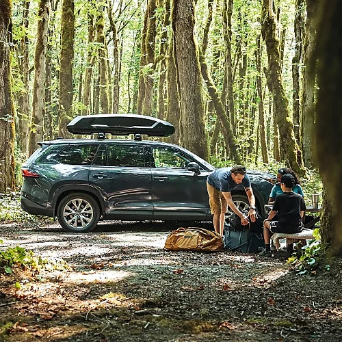 Family camping with vehicle featuring Thule Force 3 M cargo carrier in wooded area