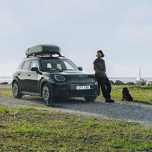 Man with dog beside SUV equipped with Thule Force 3 M cargo box on gravel road