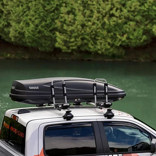 Thule 835 Hull-a-Port Pro kayak rack folded flat beside rooftop cargo box on truck – demonstrates rack compatibility and roof space saving