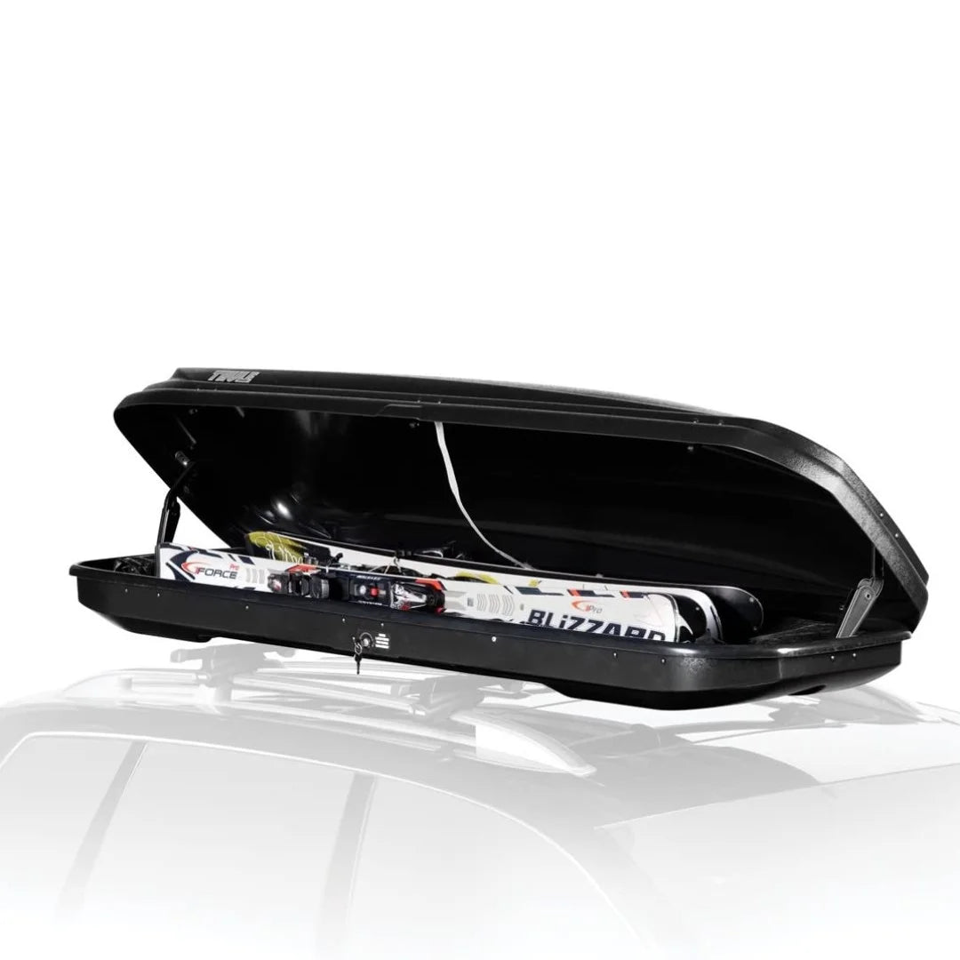 Open Thule Ascent rooftop box loaded with skis and winter gear, mounted on a vehicle for a winter trip.