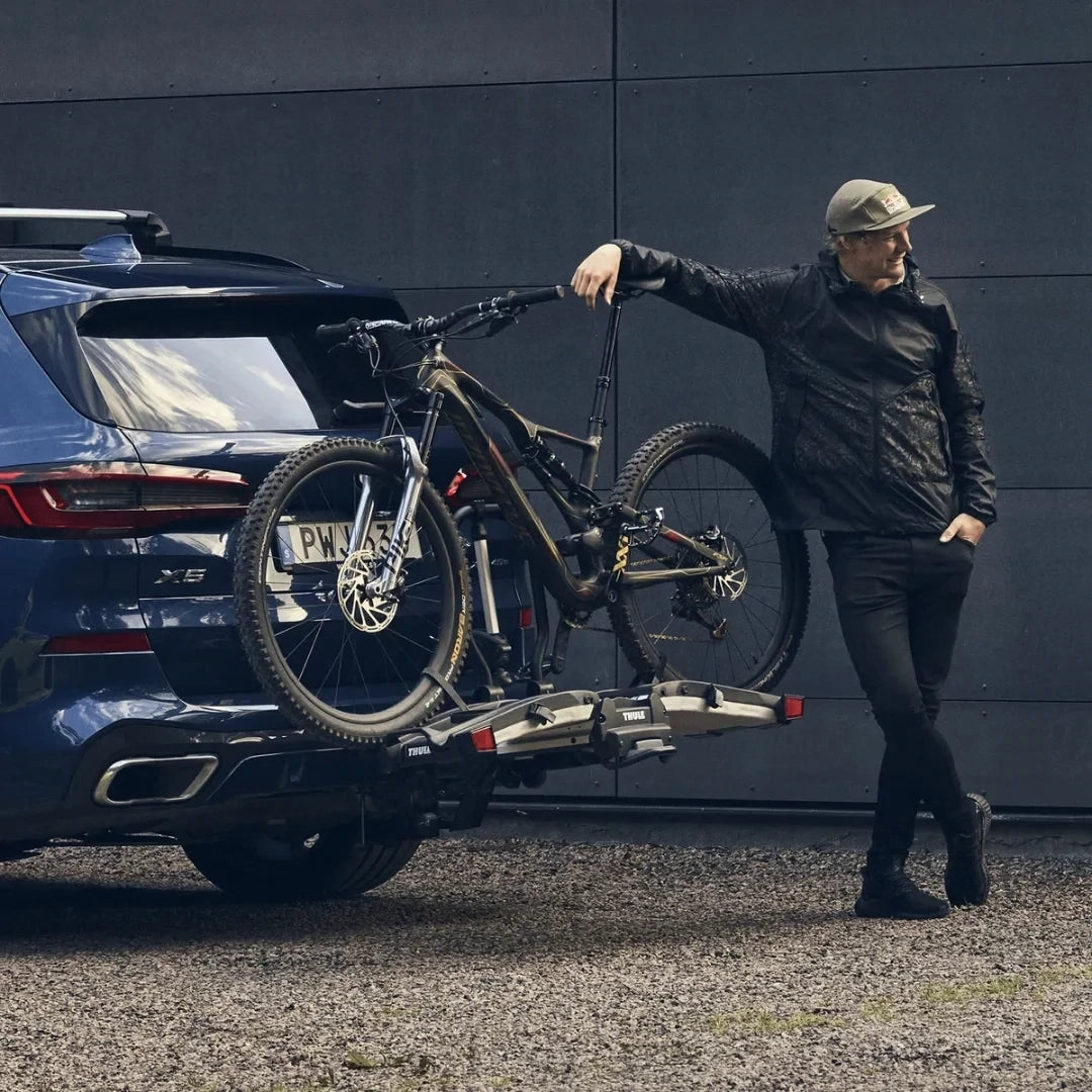 User lifting e-bike onto Thule Easyfold XT rack behind SUV