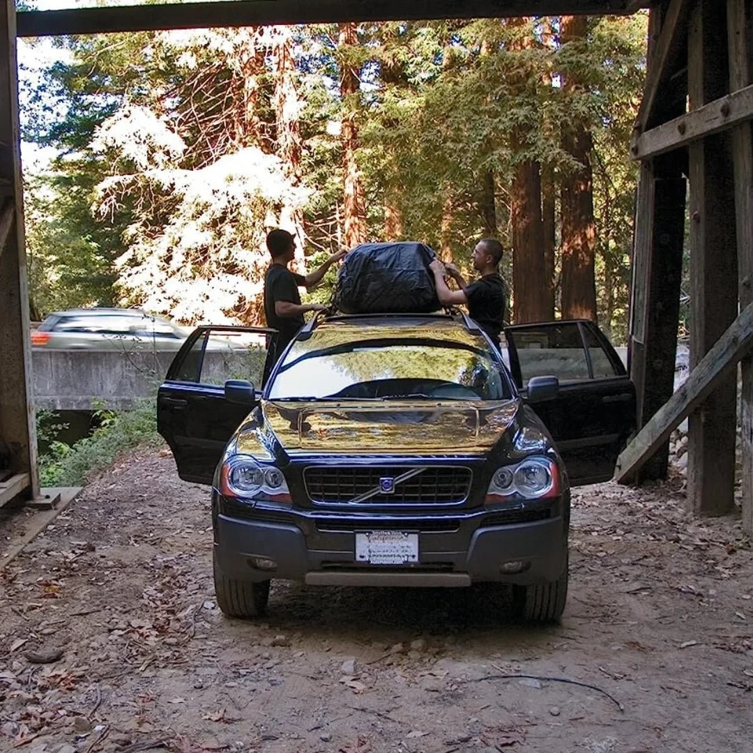SUV with Thule Escape II cargo bag installed on roof rack, driving on a dirt road surrounded by trees