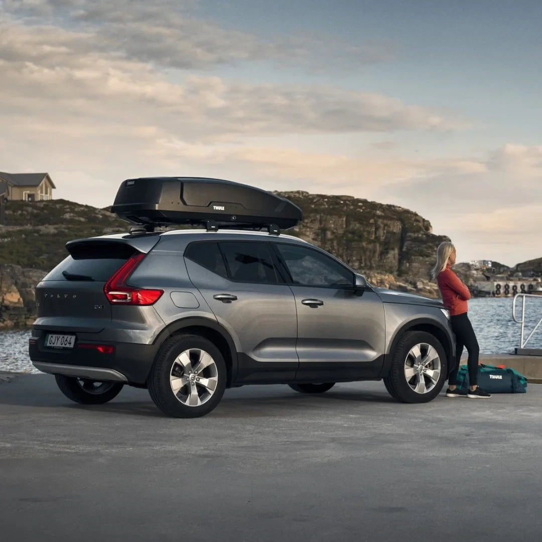 SUV parked near a scenic coastal area, equipped with a Thule Force XT Sport cargo box.