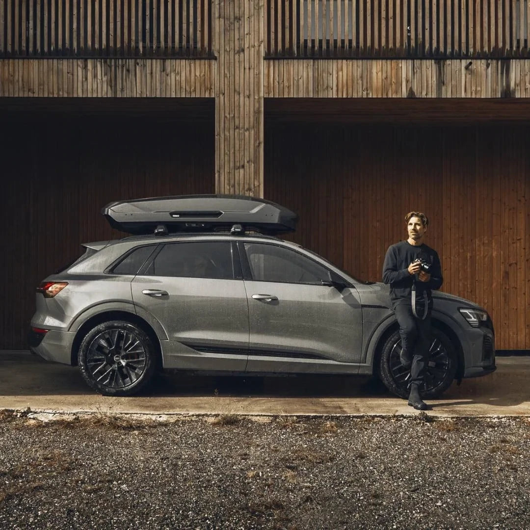 Thule Motion 3 Cargo Box installed on a car. A person with a camera leaning on it.