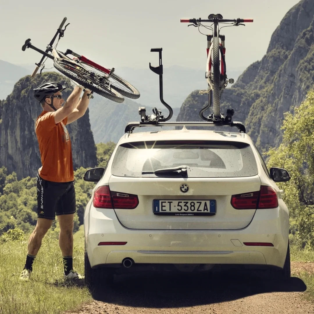 Person securing bikes onto a car using Thule ProRide XT roof racks with mountains in the background