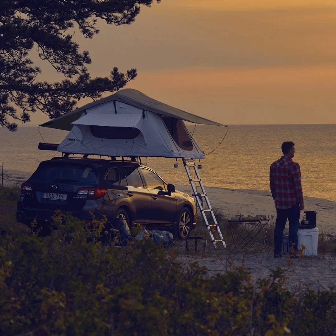 Thule Tepui Low-Pro Rooftop Tent on top of parked car. Man looking over ocean in sunset