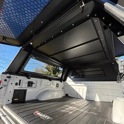 Interior of stainless steel canopy for Dodge Ram 1500 and Ram Classic 5.7' bed with reinforced gullwing side doors, shown on Ford F150 for reference.