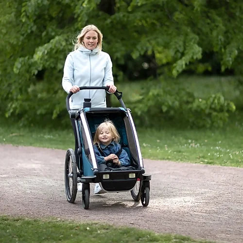 Parent walking outdoors with Thule Chariot Cross Single Majolica Blue stroller carrying a happy child