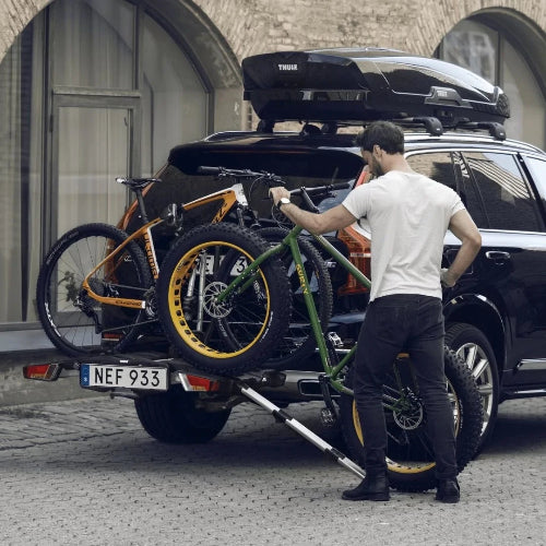 Person rolling fat bike onto car rack using ramp