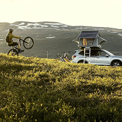 Thule Tepui Ayer 2 rooftop tent on SUV parked in mountain landscape with cyclist riding nearby