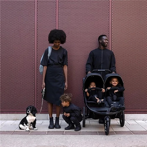 Family walking with Thule Urban Glide 3 double stroller carrying two children while a dog sits beside them