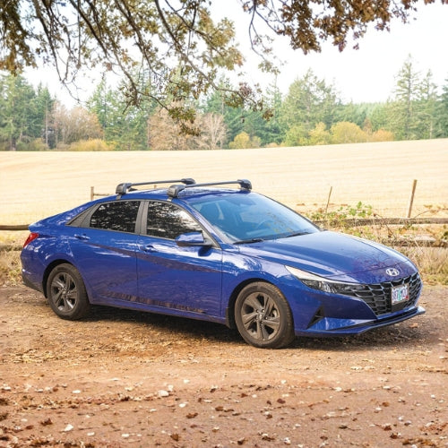 Blue car parked on a dirt road with trees and fields in the background