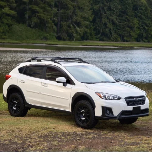 White SUV with black roof rack parked by a lake with trees in the background