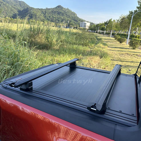 Black lockable bed rack crossbars mounted across a retractable hard tonneau cover on a pickup truck bed.