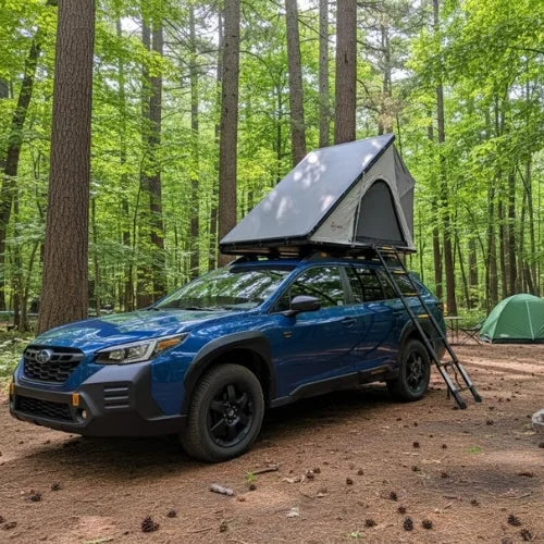 Blue SUV with a rooftop tent in a forest setting with a ground tent in the background