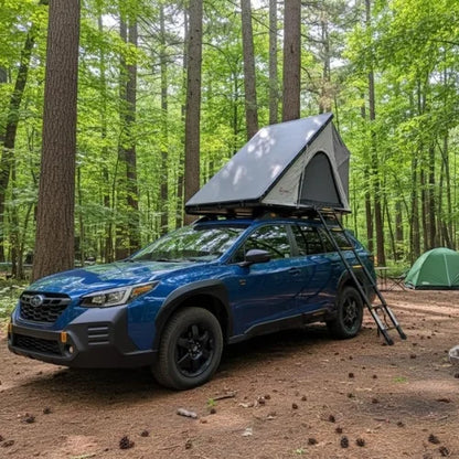 Blue SUV with a rooftop tent in a forest setting with a ground tent in the background