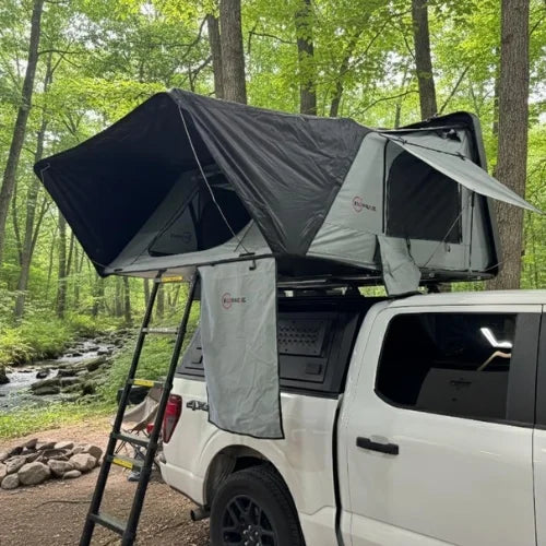 Roof top tent attached to a white truck in a forest setting