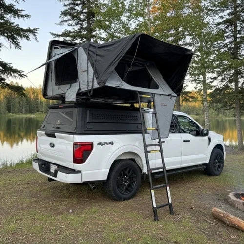 White 4x4 truck with a canopy roof rack and a open rooftop tent in a forest setting