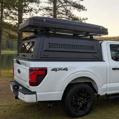 White 4x4 truck with a canopy roof rack and a closed rooftop tent in a forest setting