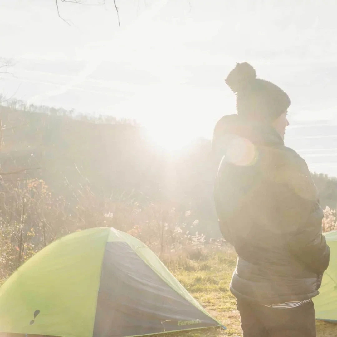 Lifestyle image of a person outdoors, standing next the Eureka Suma tent in natural sunlight.