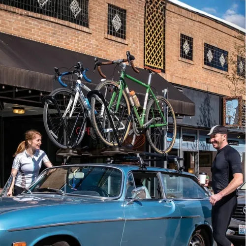 Two bicycles on a car roof rack with a brick building in the background