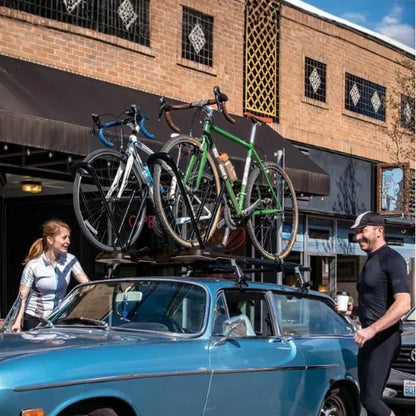 Two bicycles on a car roof rack with a brick building in the background