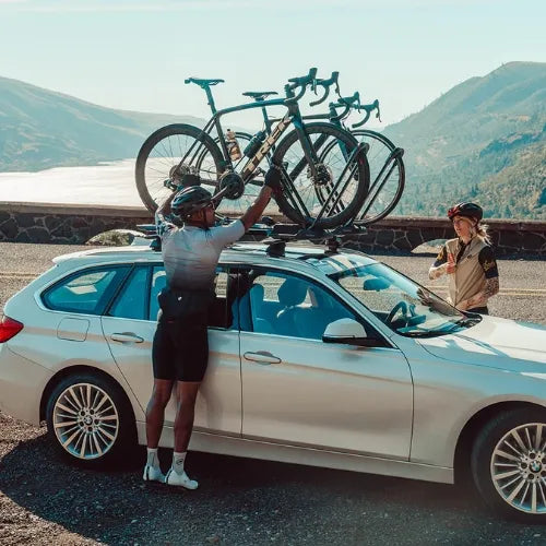 Two people loading bicycles onto a car with mountains in the background
