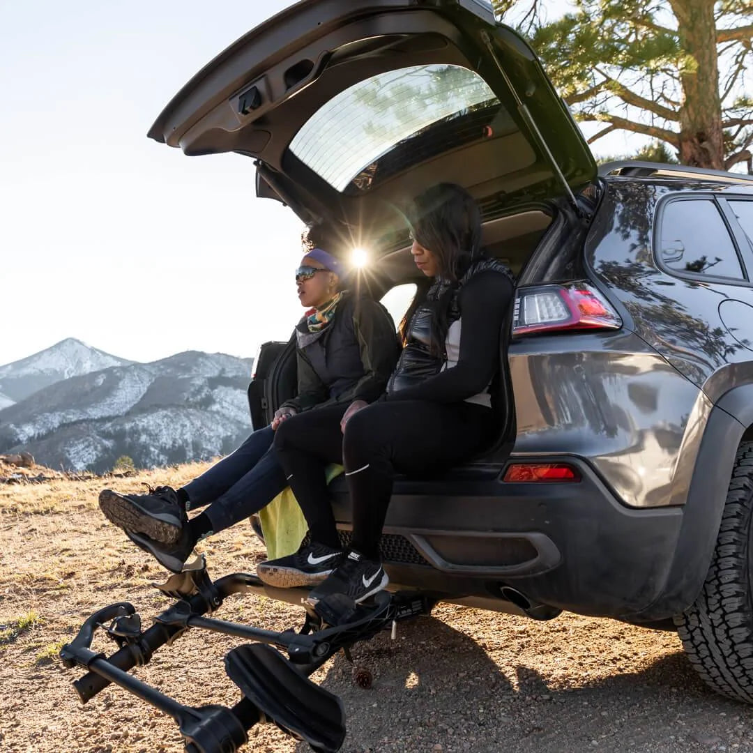 Two people sitting on the open tailgate of an SUV with Kuat rack folded down