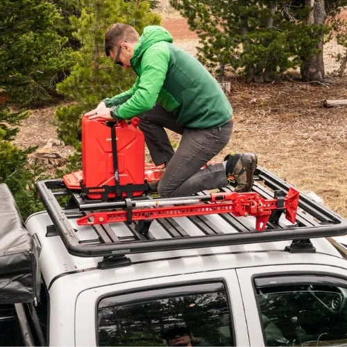 Person installing a red roof rack system on a vehicle in a forested area.