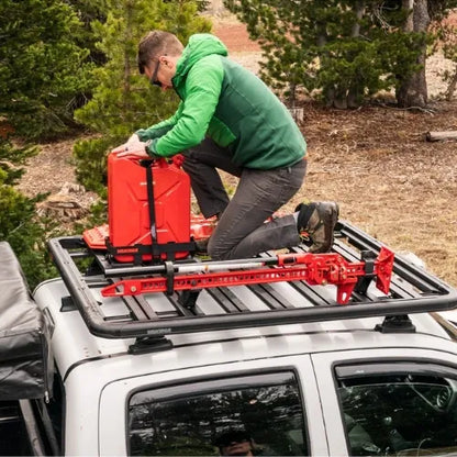 Person installing a red roof rack system on a vehicle in a forested area.