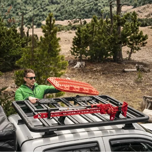 Man loading a red roof rack onto a vehicle in a natural setting