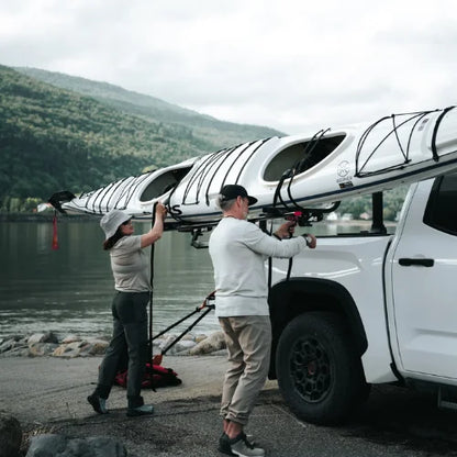 MOS UpLift™ Universal Lift Assist Rack System installed on a truck bed rack with lake and hill in the background and with someone loading a tandem kayak which is tilted down
