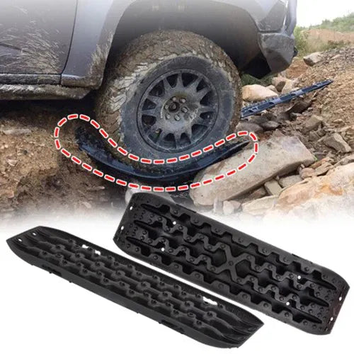 Black recovery traction boards deployed under off-road vehicle tire stuck in mud.

