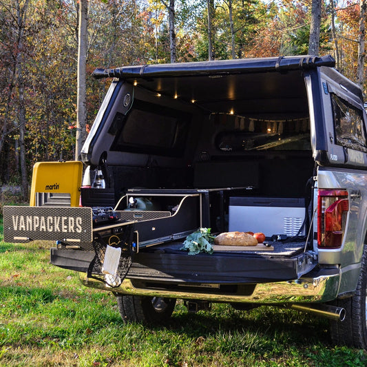 truck with open cargo area in a forest setting, featuring Vanpackers branding.