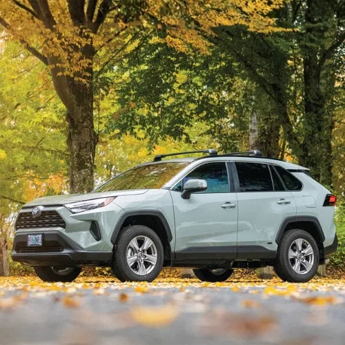 Light blue Toyota SUV parked on a road lined with trees with autumn foliage.