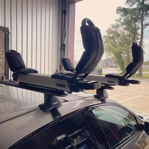 Thule Hullavator Pro  Thule rack mounted on a car roof with a building and trees in the background.