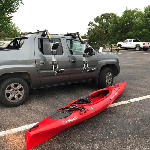 Thule Hullavator Pro Red kayak on the ground next to a gray truck with kayak holders in a parking lot.