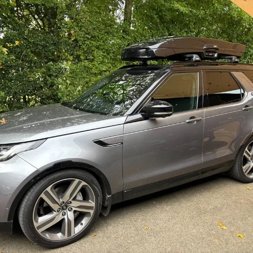 Silver SUV with a roof rack parked on a road with trees in the background