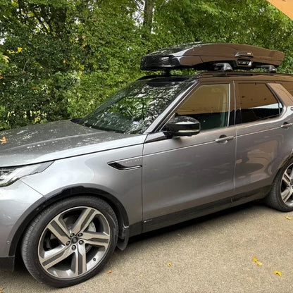 Silver SUV with a roof rack parked on a road with trees in the background