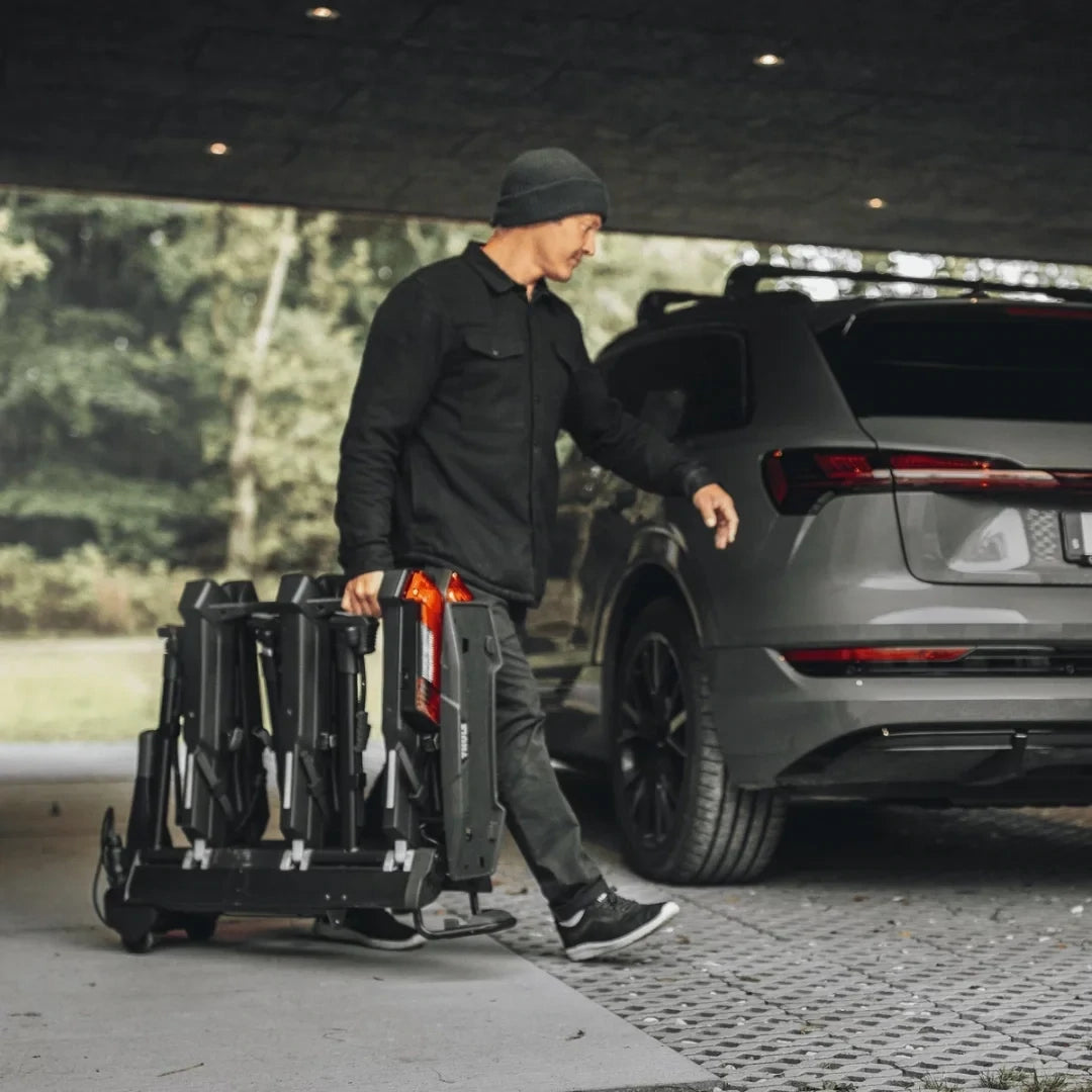 User carrying the folded Thule Epos rack behind a parked SUV