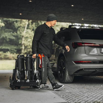 User carrying the folded Thule Epos rack behind a parked SUV