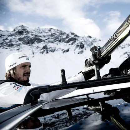 Man attaching cross-country skis to car roof rack with Thule SkiClick in snowy mountain setting