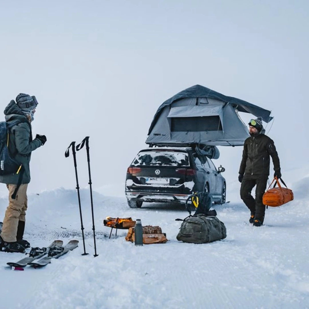 Tent in snowy setting with people and gear around vehicle