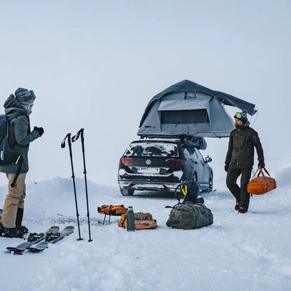 Tent in snowy setting with people and gear around vehicle